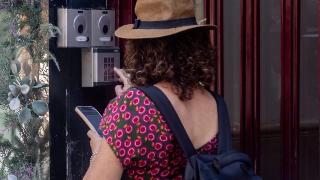 Mujer usando su teléfono frente a un intercomunicador en un edificio.