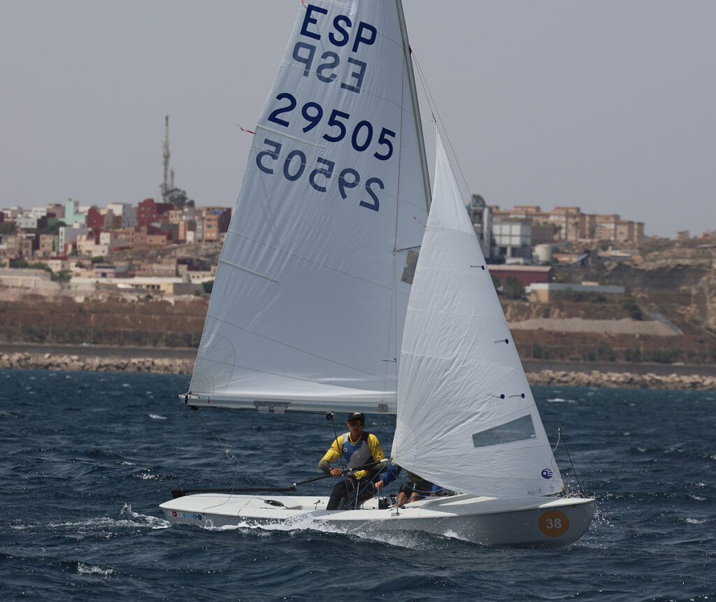 Dos regatistas navegando en un velero durante una competición con viento fuerte.