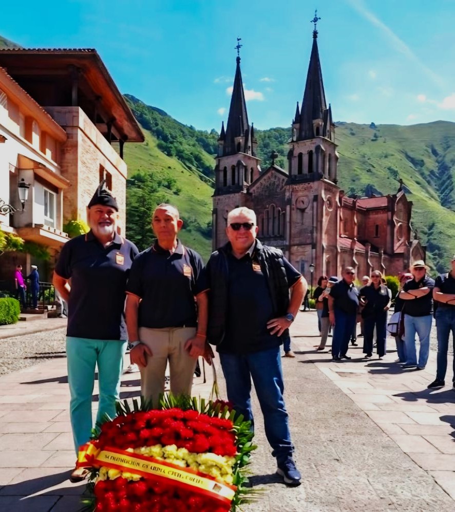Tres hombres junto a una ofrenda floral en un evento conmemorativo.