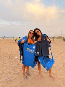 Dos mujeres sonrientes sosteniendo camisetas en la playa de San Lorenzo