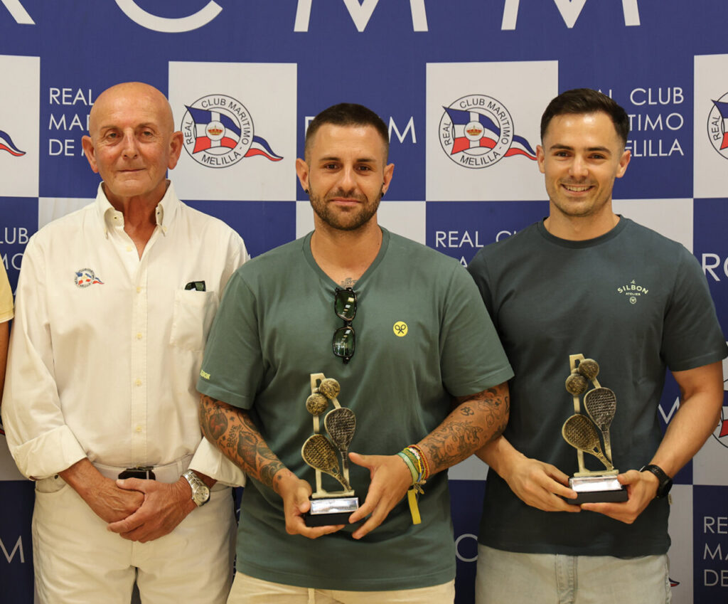 Three men pose together, two of them holding trophies at an awards event in front of a blue-and-white club backdrop.