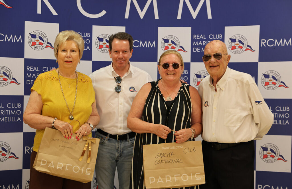 Group photo of four people at a Real Club Marítimo de Melilla event, posing in front of a blue-and-white backdrop with logos.