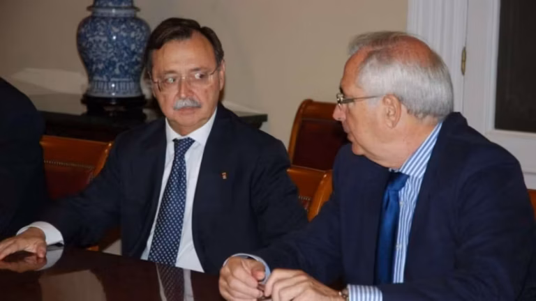 Two men in suits seated at a conference table, engaged in a discussion.