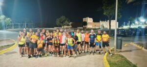 Group of runners posing together at night on a paved area, wearing bright athletic gear with a historic building in the background.