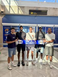 Jugadores del Club Melilla Baloncesto sosteniendo una bufanda en el aeropuerto