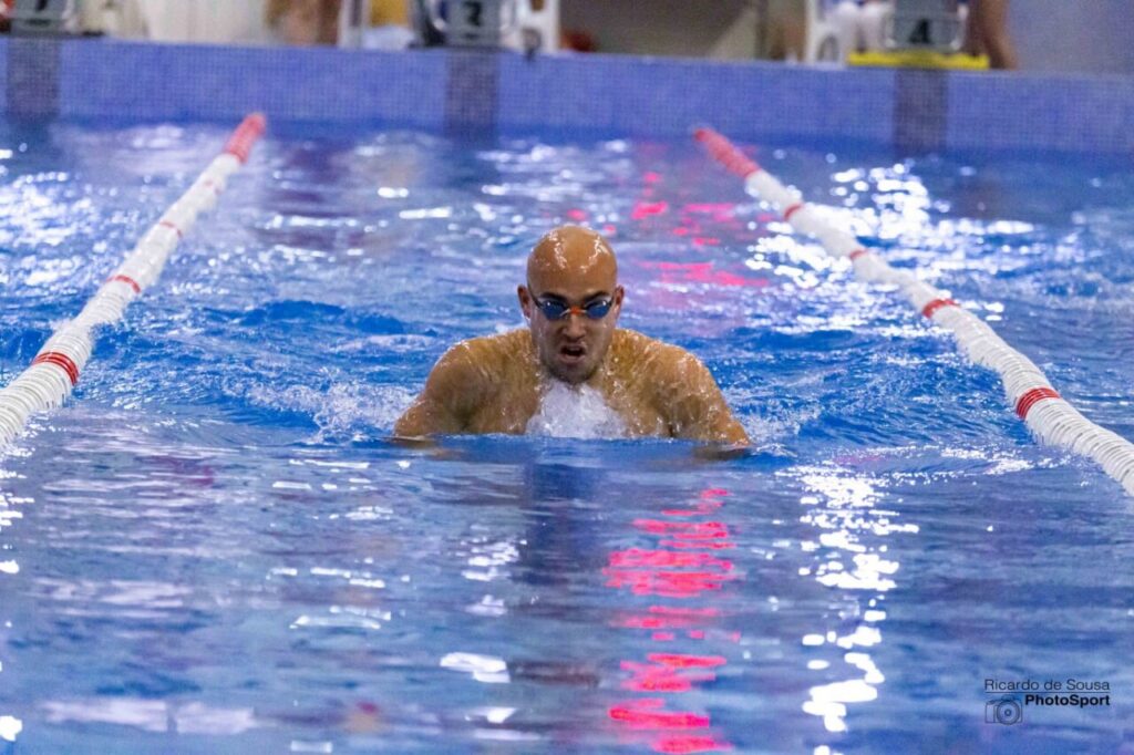 Male swimmer emerges from the water at the end of a race, wearing goggles and blue lane markers nearby.