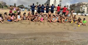Grupo de niños disfrutando en la playa durante un campamento de verano.