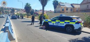 Policía local realiza un control de tráfico en una avenida, con una patrulla y dos agentes de pie junto al coche.