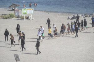 Grupo de personas migrantes en la playa de Ceuta con presencia policial