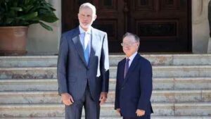 Two men in formal suits stand side by side on marble steps in front of a large wooden door.