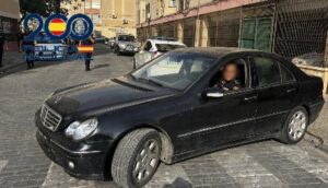 Black sedan parked on a cobblestone street with a blurred driver visible; a blue-and-white '200' anniversary banner in the background.