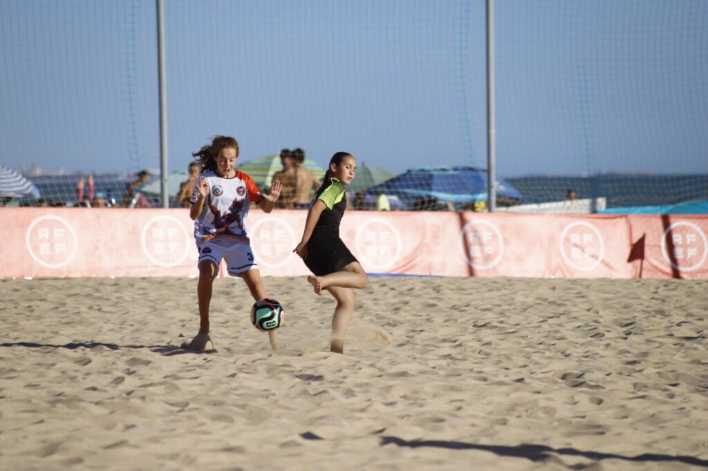 Jugadoras de fútbol playa infantil compitiendo en la arena.