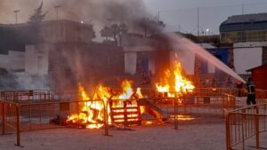 Hogueras de San Juan con llamas y bomberos apagando el fuego