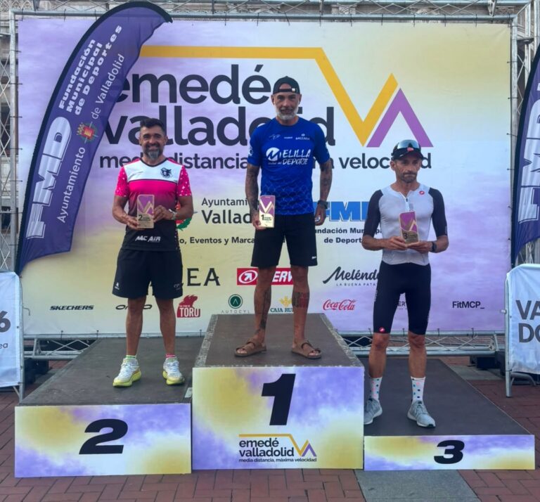 Three male winners stand on a podium holding plaques: 1st place center, 2nd on the left, 3rd on the right, with a colorful event backdrop behind them.