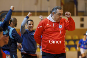 Man in a red hoodie pumps a fist in celebration as teammates cheer in a gym.
