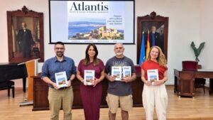 Four adults stand in a formal room, each holding an Atlantis magazine, in front of a screen displaying the magazine cover.
