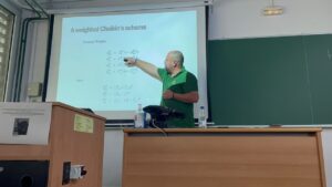 Lecturer in a green shirt explains a slide titled 'A weighted Chaikin's scheme' with equations in a classroom.