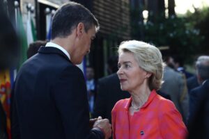 Man in a dark suit and a woman in a pink blazer talk privately at an outdoor event.|Outdoor event conversation between professionals