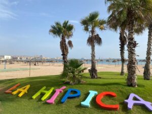 Colorful 3D letters spelling 'LA HIPICA' on a grassy beach park with palm trees and beach umbrellas in the background.