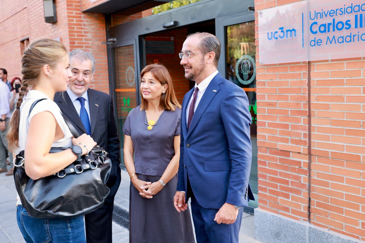 Inicio de curso de la Princesa Leonor - MelillaHoy Four professionals in business attire stand outside a brick UC3M Madrid building, chatting near the entrance,