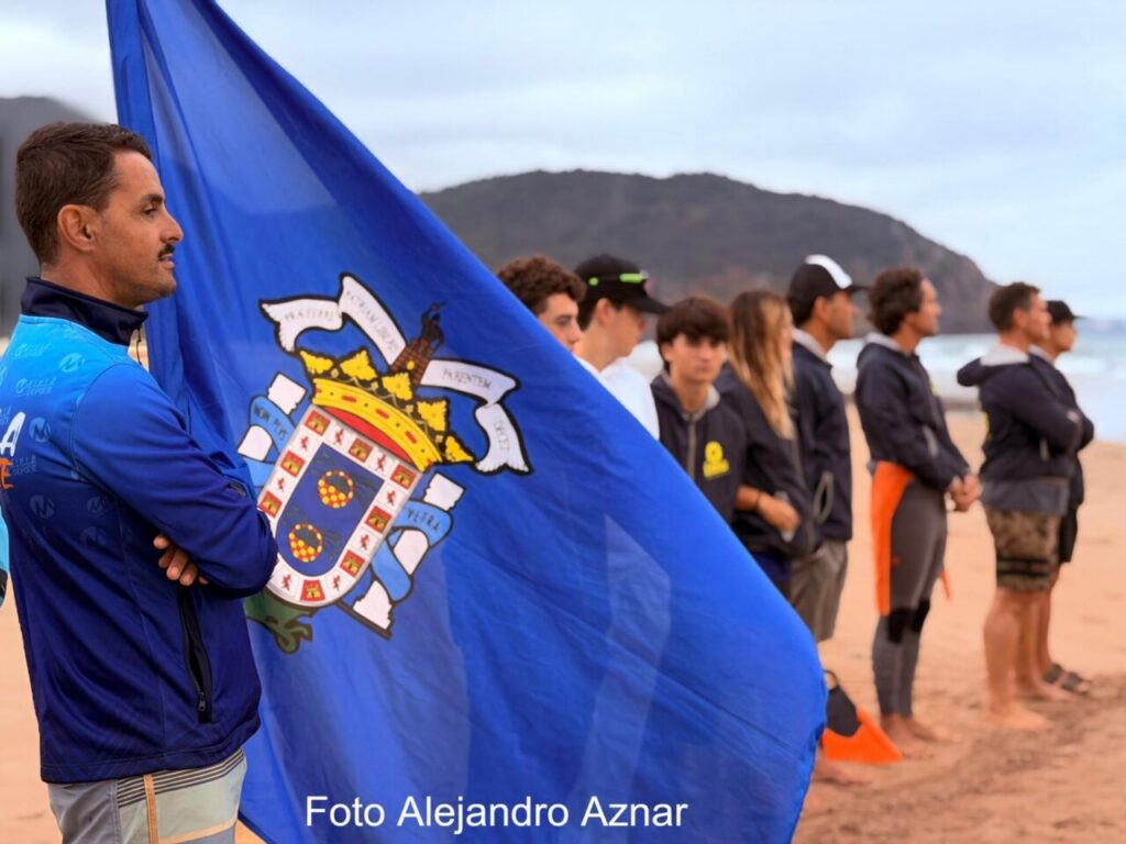Competidores de surf en la playa con bandera de Melilla