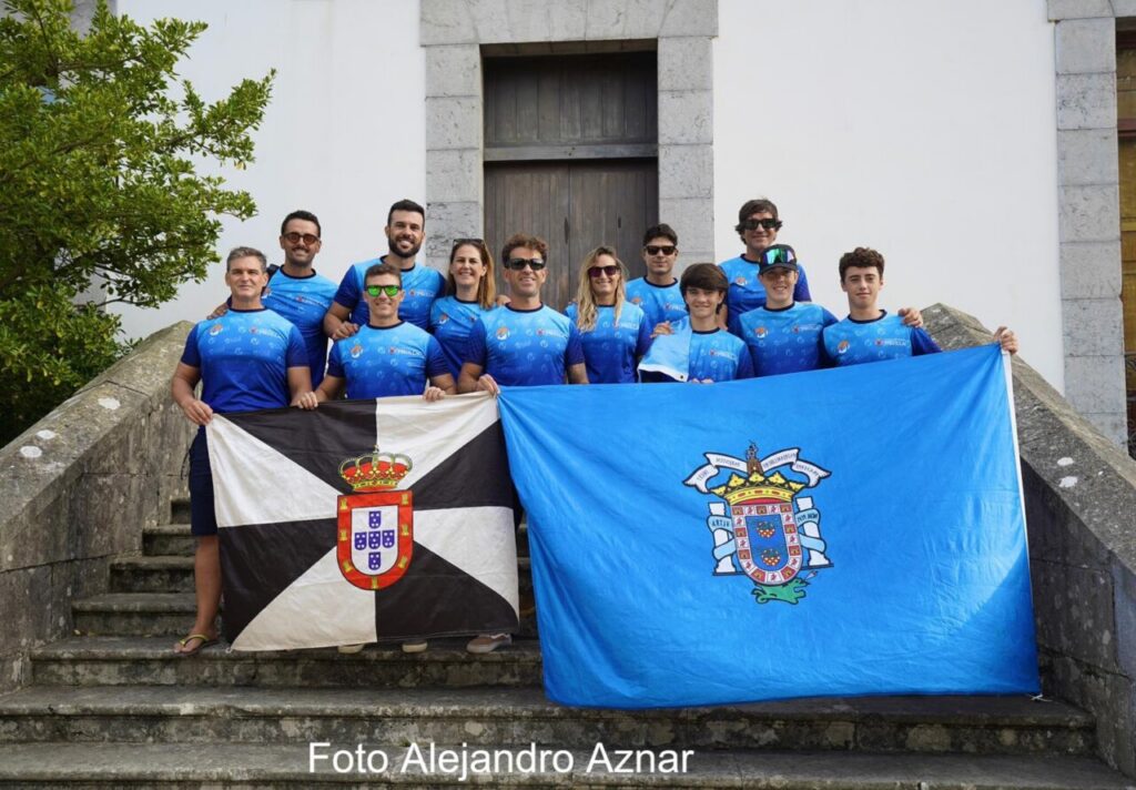 Group of people in blue shirts pose on stone steps, holding Portugal and blue crested flags.