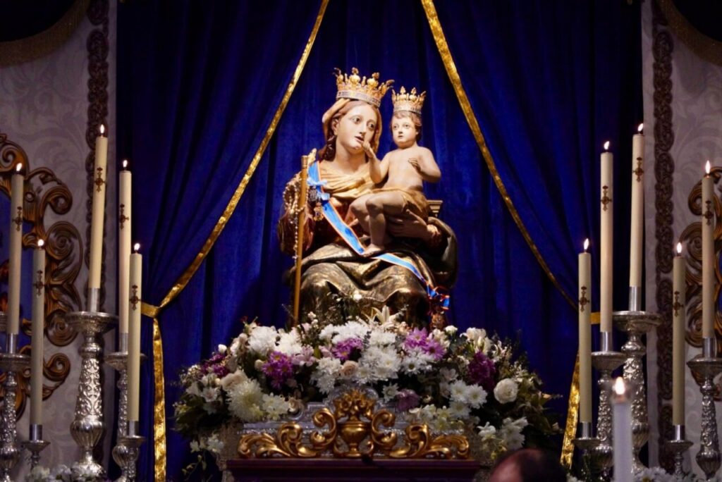 Estatua de la Virgen de la Victoria con flores y velas en misa