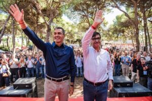 Dos políticos saludando a una multitud en un acto al aire libre