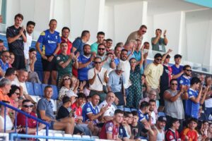 Crowd of sports spectators in stadium seating, many clapping and cheering for a game.