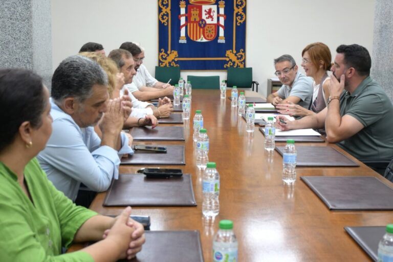 Group of adults seated around a long conference table in a formal meeting room, with bottled water and folders on the table.