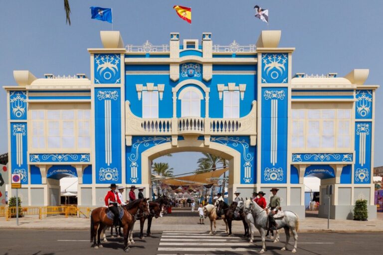 Blue ornate arch gateway with white decorative patterns, riders on horses in front at a crosswalk during a festival.