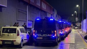 Line of police vans with blue emergency lights at night on a narrow urban street