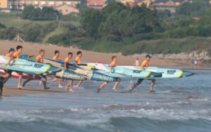 Grupo de deportistas corriendo con tablas de SUP en la playa