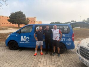 Tres hombres posando junto a un vehículo de Melilla Ciclismo en un evento de MTB.