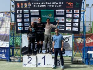 Three men stand on a winners' podium (1st, 2nd, 3rd) posing after a MTB race, with a sponsor banner in the background titled Copa Andaluza de Enduro MTB 2025.