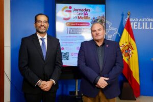 Two men in suits pose in front of a poster about AI conferences, with a Spanish flag nearby.