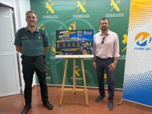 Dos hombres posando junto a un cartel de evento motero de la Guardia Civil en Melilla.