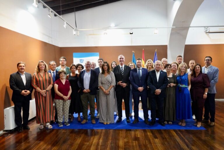 Group of 20+ professionals in formal attire posing for a group photo on a blue carpet in a conference room with flags in the background.
