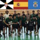 Youth sports team in green uniforms posing for a group photo in an indoor gym, with coaches at either end and flags overhead (including Portugal and Spain).