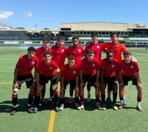 Youth soccer team posing for a group photo on a green field, all wearing red jerseys and black shorts.