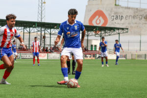 Soccer player in blue jersey dribbles the ball on a green field as opponents in red-and-white stripes close in.