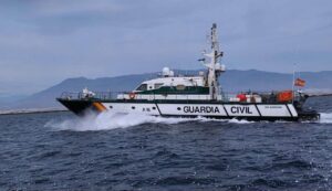 Spanish Guardia Civil patrol boat (A16) speeds across the sea with a mountainous coast in the background, white hull with green stripe and 'GUARDIA CIVIL' along the side.