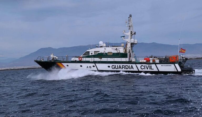 Spanish Guardia Civil patrol boat (A16) speeds across the sea with a mountainous coast in the background, white hull with green stripe and 'GUARDIA CIVIL' along the side.