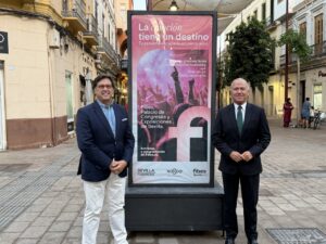 Dos hombres posando frente a un cartel de promoción turística en Sevilla