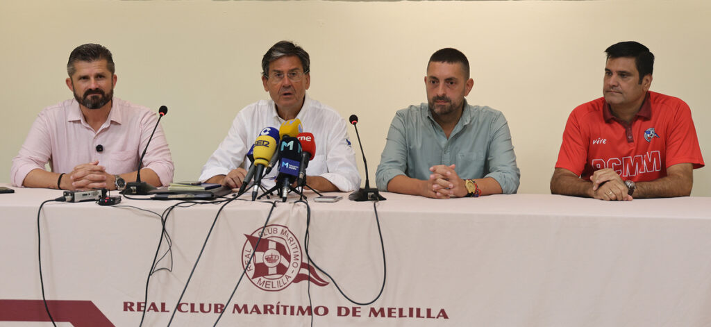 Panel of four men seated at a press conference table with multiple microphones; banner reads Real Club Marítimo de Melilla in the foreground.