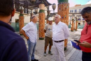 Group of men standing and talking in a tiled outdoor area with mosaic columns; one man wears a hard hat, suggesting a construction or inspection scene.