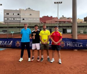 Four men on a red clay tennis court pose with trophies after a match, with a Melilla banner in the background.