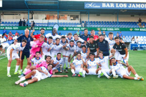 Jugadores de la U.D. Melilla celebrando en el campo con su entrenador