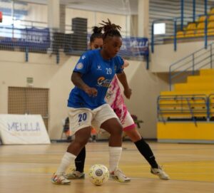 Futsal players duel for the ball on an indoor court; blue jersey #20 challenges a pink‑kit opponent.