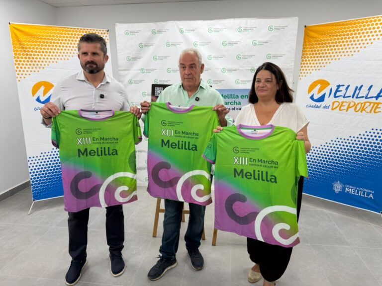 Three people hold bright green race jerseys that read XIII En Marcha Melilla, standing in a room with event backdrops.